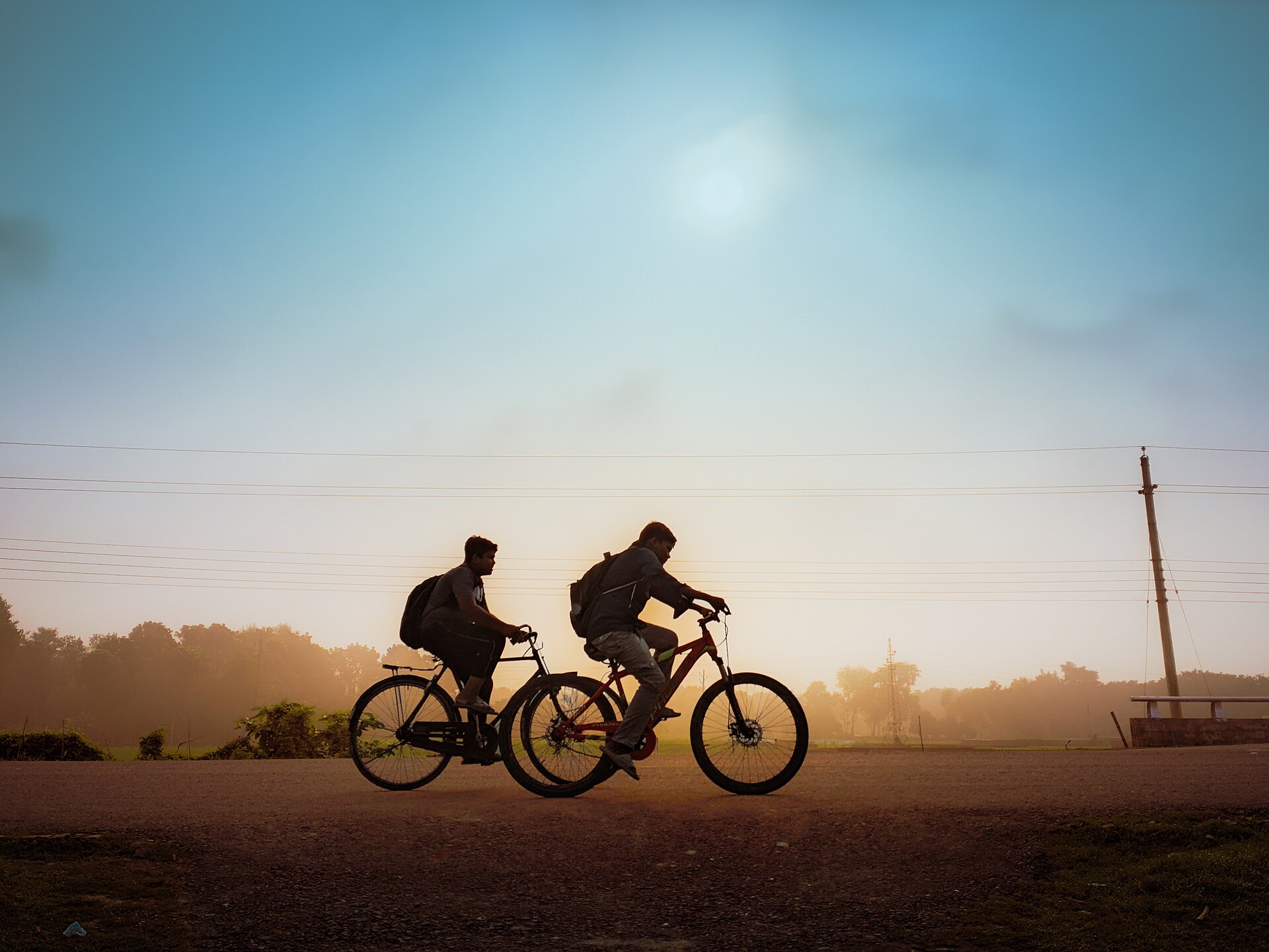 Two students riding bicycles to school at sunrise in rural Bangladesh
