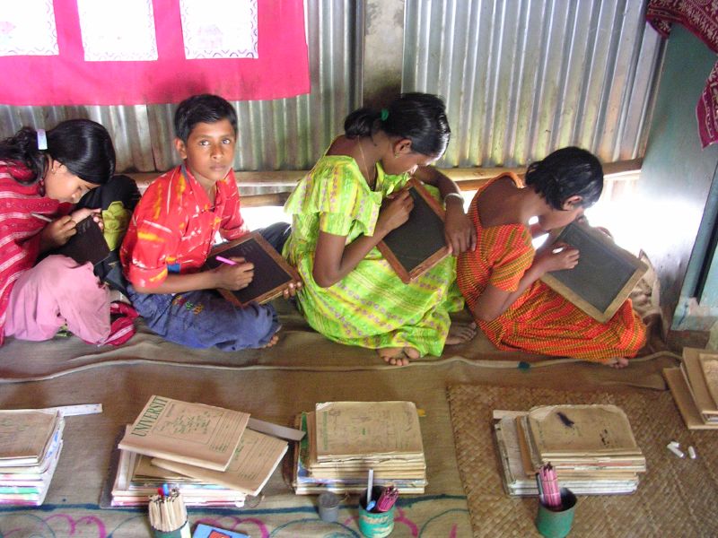 Children studying together on the floor with slates and notebooks in a rural Bangladeshi classroom